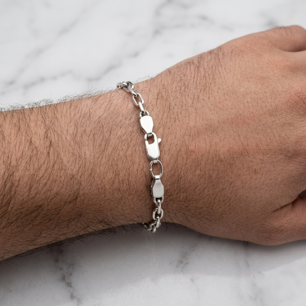 Nahaufnahme eines geschwärzten Ankerarmbands aus 925er Sterlingsilber mit Karabinerverschluss am Handgelenk eines Mannes vor einem hellen Marmorhintergrund.