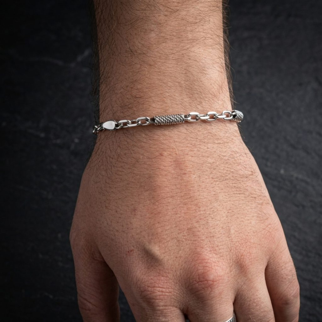 Nahaufnahme eines oxidierten Ankerarmbands из 925er Sterlingsilber mit Seildraht-Einsätzen und Karabinerverschluss an einem Handgelenk vor einem dunklen Hintergrund.