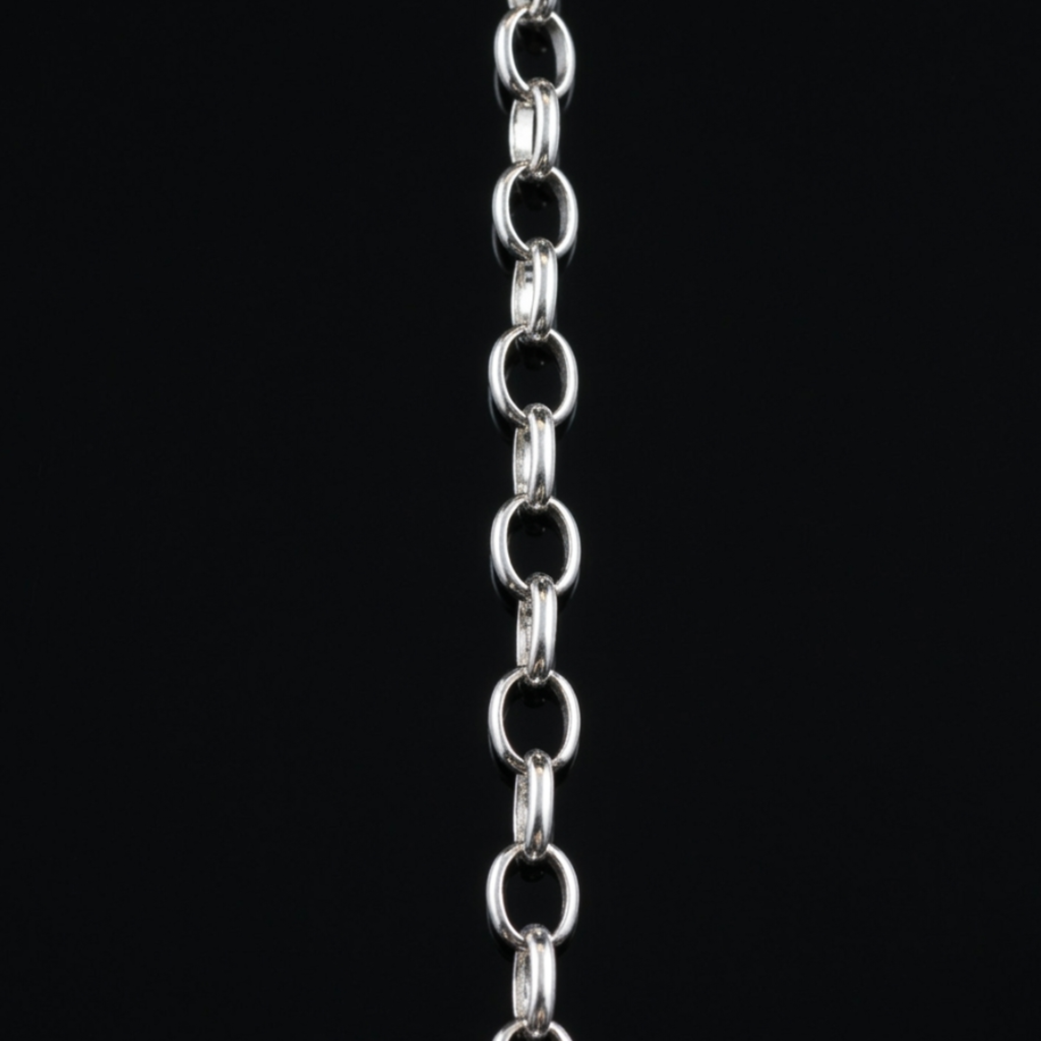 Detailansicht einer silbernen Gliederkette im Rolo-Stil, die sich auf einem dunklen, reflektierenden Hintergrund spiegelt.