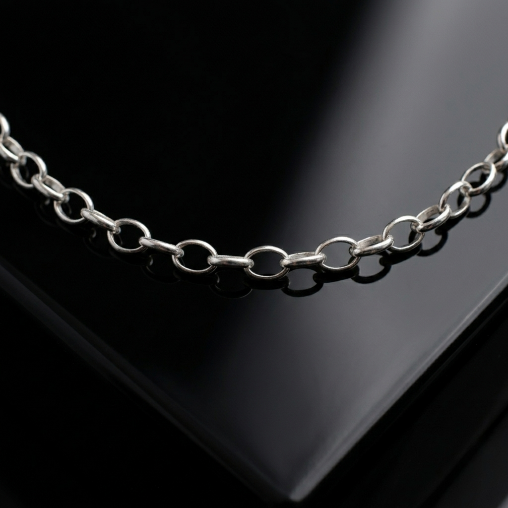 Makroaufnahme einer glänzenden Rolo-Kette (Ankerkette) aus 925er Silber auf einer spiegelnden, schwarzen Oberfläche mit eleganten Lichtreflexen.