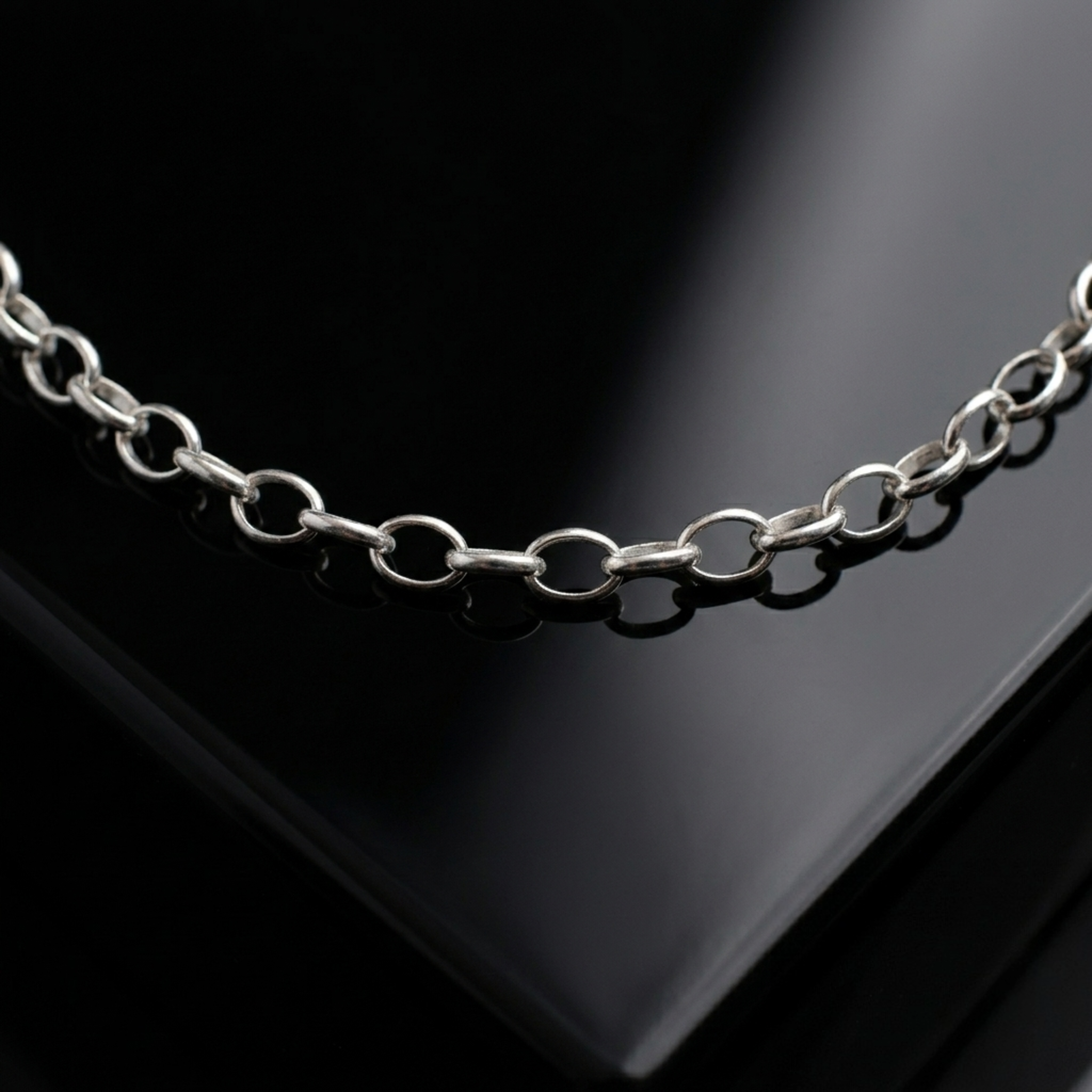 Makroaufnahme einer glänzenden Rolo-Kette (Ankerkette) aus 925er Silber auf einer spiegelnden, schwarzen Oberfläche mit eleganten Lichtreflexen.