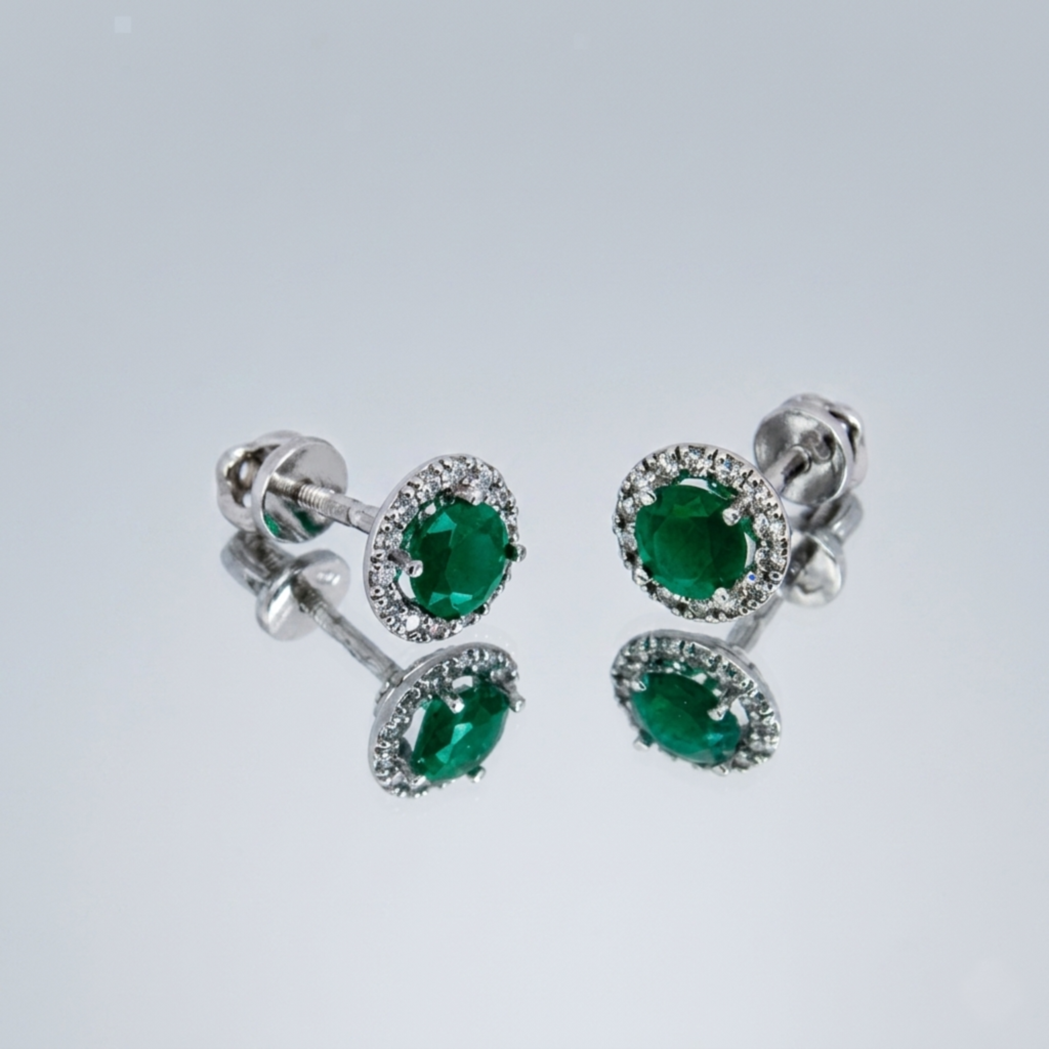 Ein Paar 925 Sterling Silber Halo-Ohrstecker rhodiniert mit grünem Zirkonia-Stein und Schraubverschluss auf einer Spiegeloberfläche.