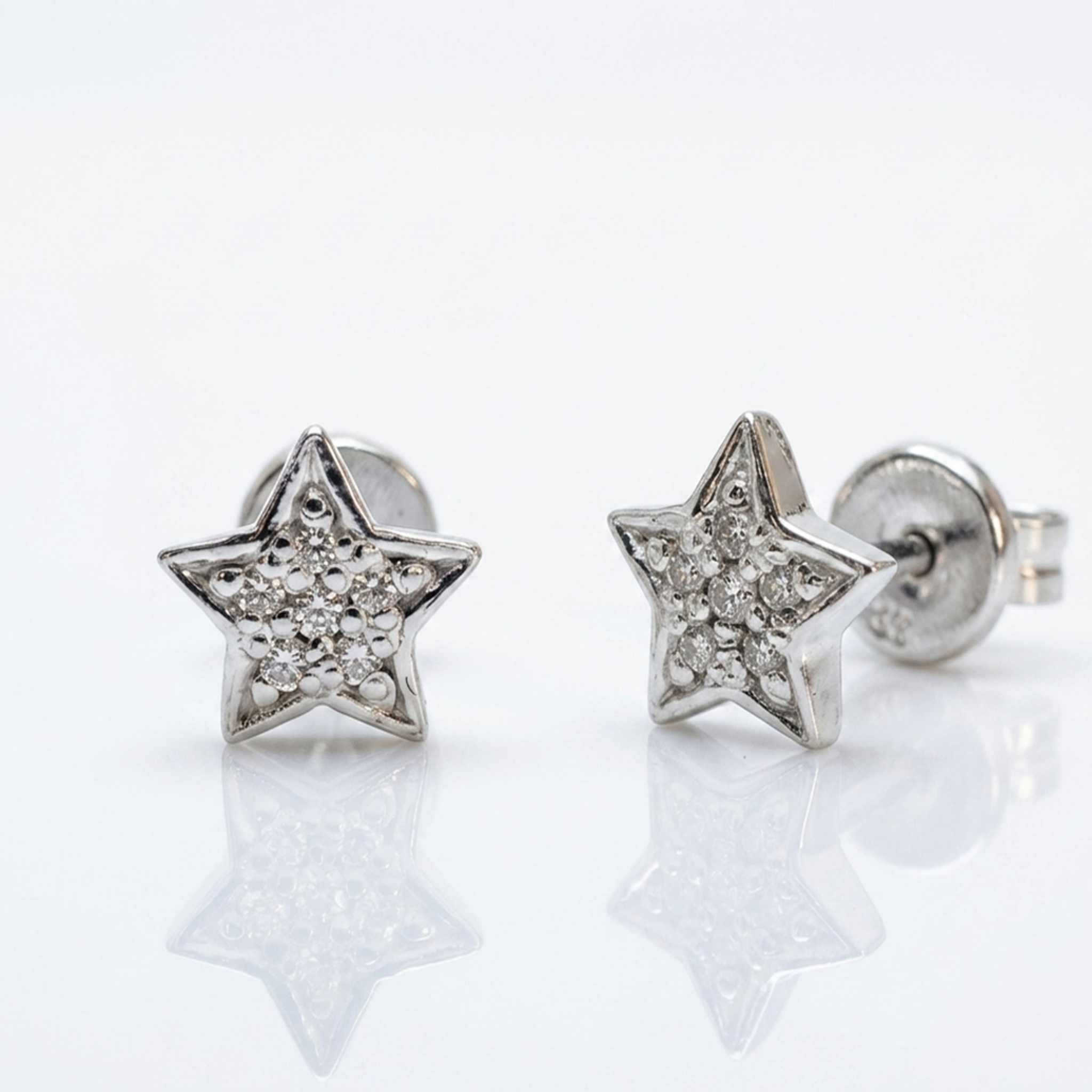 Nahaufnahme von filigranen fünfzackigen Stern-Ohrringen aus Sterlingsilber 925, die Innenfläche komplett mit kleinen weißen Zirkonia-Steinen besetzt, freigestellt auf weißem Boden.