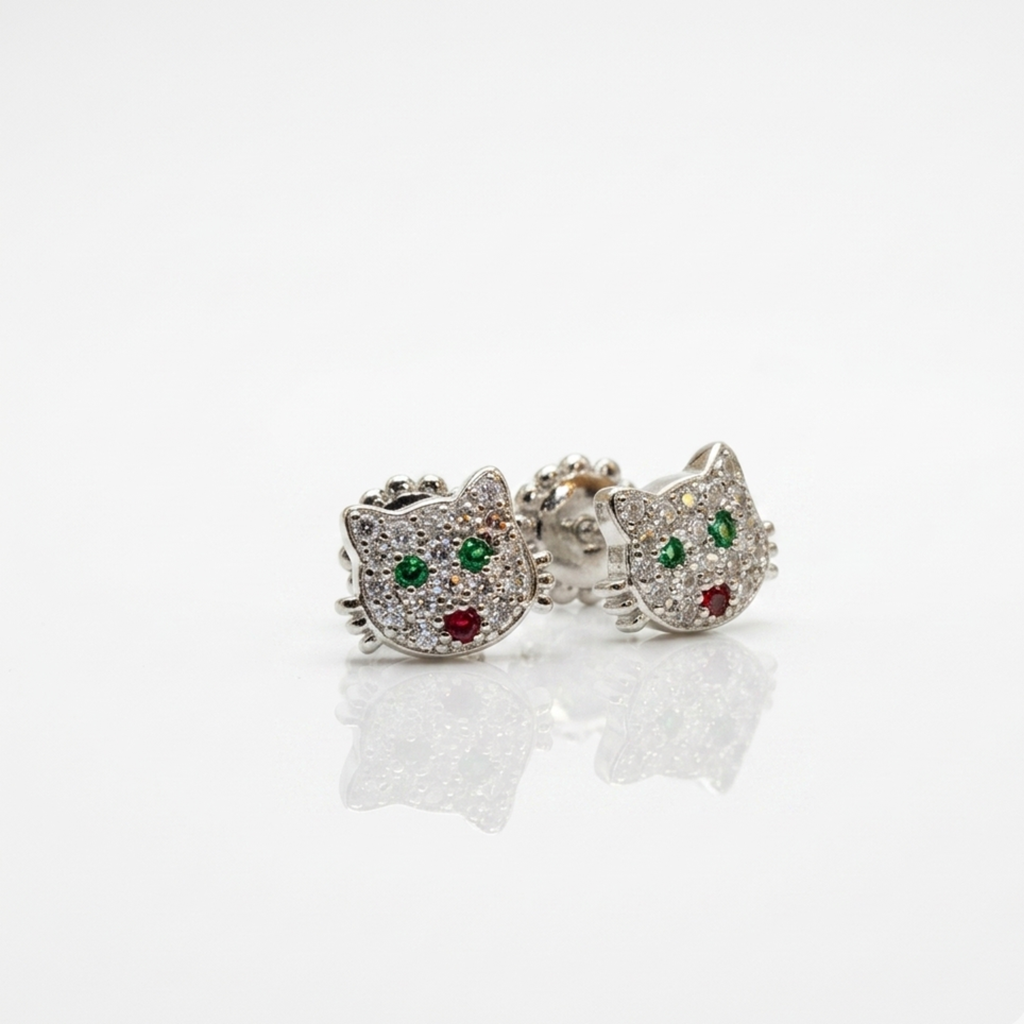 Ein Paar silberne Ohrringe im Hello-Kitty-Design mit funkelnder Zirkonia-Besetzung, flach liegend auf einer weißen glatten Oberfläche mit einer leichten Spiegelung.