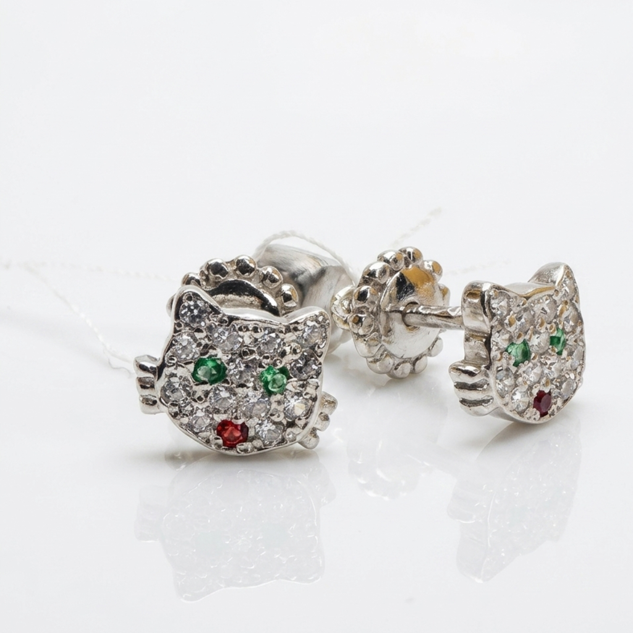 Nahaufnahme von filigranen Ohrringen из Sterlingsilber 925, das Katzen-Motiv komplett mit kleinen weißen, grünen und roten Zirkonia-Steinen besetzt, freigestellt auf weißem Boden.