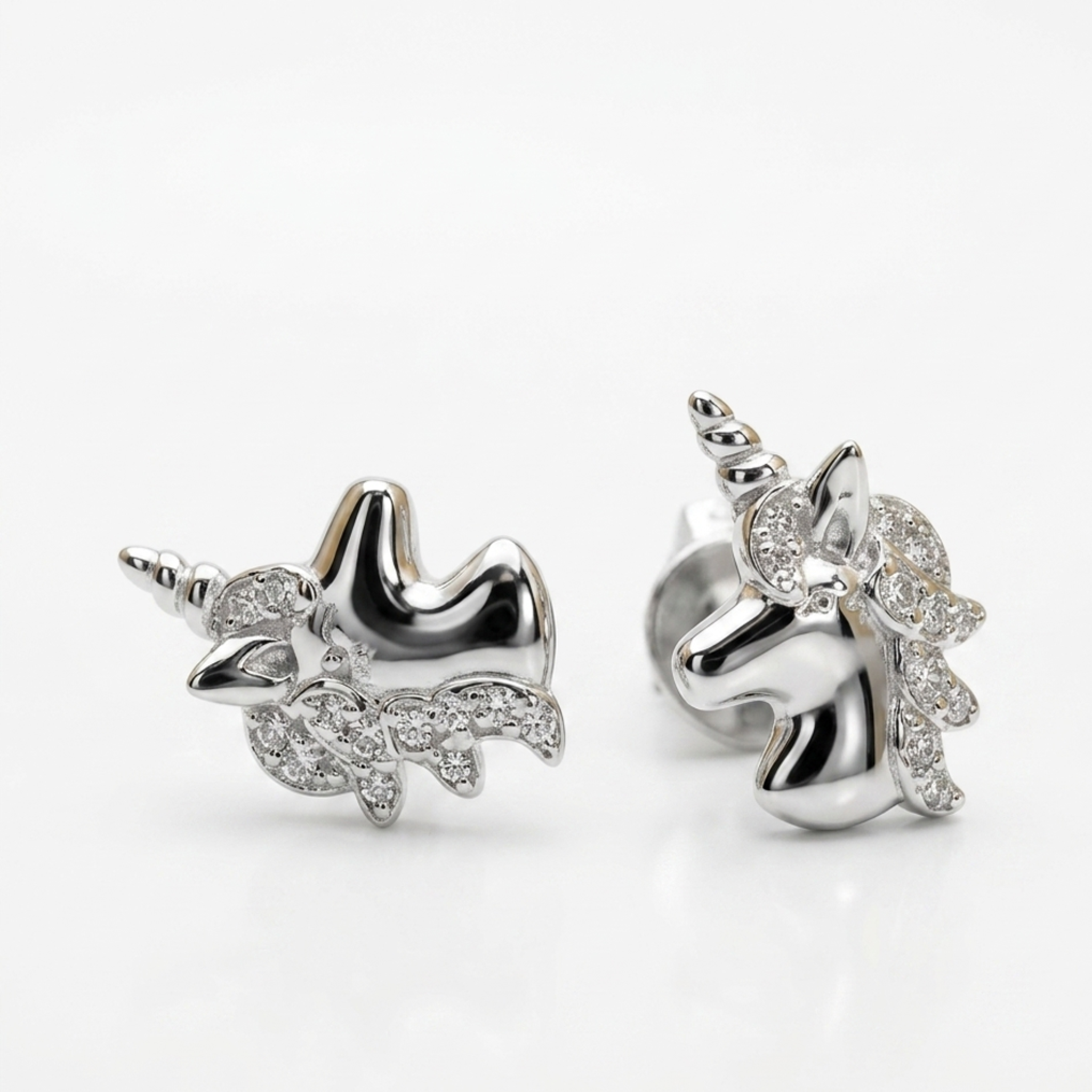 Makroaufnahme von paarigen Silberohrringen in Einhorn-Form aus 925er Sterling Silber, rhodiniert, spiegelsymmetrisch angeordnet auf weißer Studio-Oberfläche.
