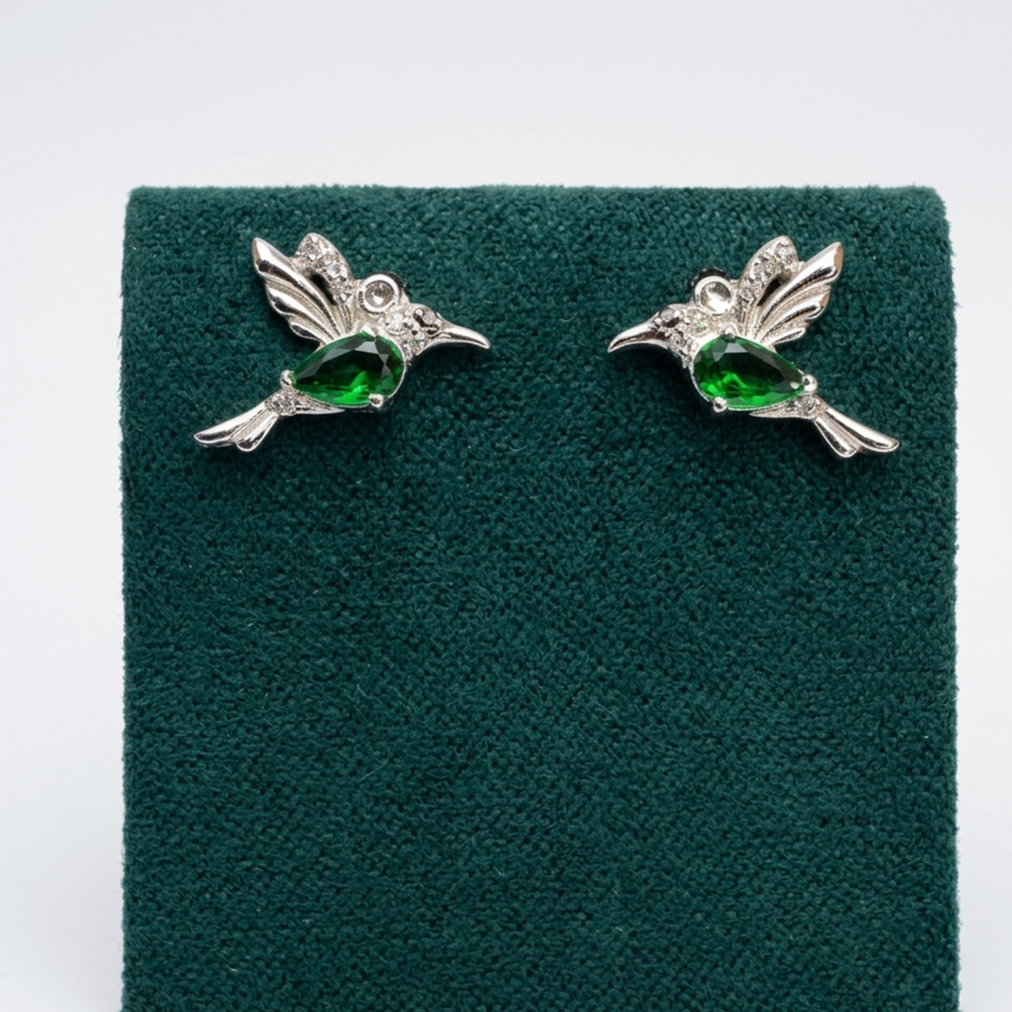 Nahaufnahme der luxuriösen Vogel-Ohrringe aus 925er Sterling Silber mit Rhodium-Anlaufschutz und glitzerndem Zirkonia-Besatz auf einem edlen grünen Samtaufsteller.