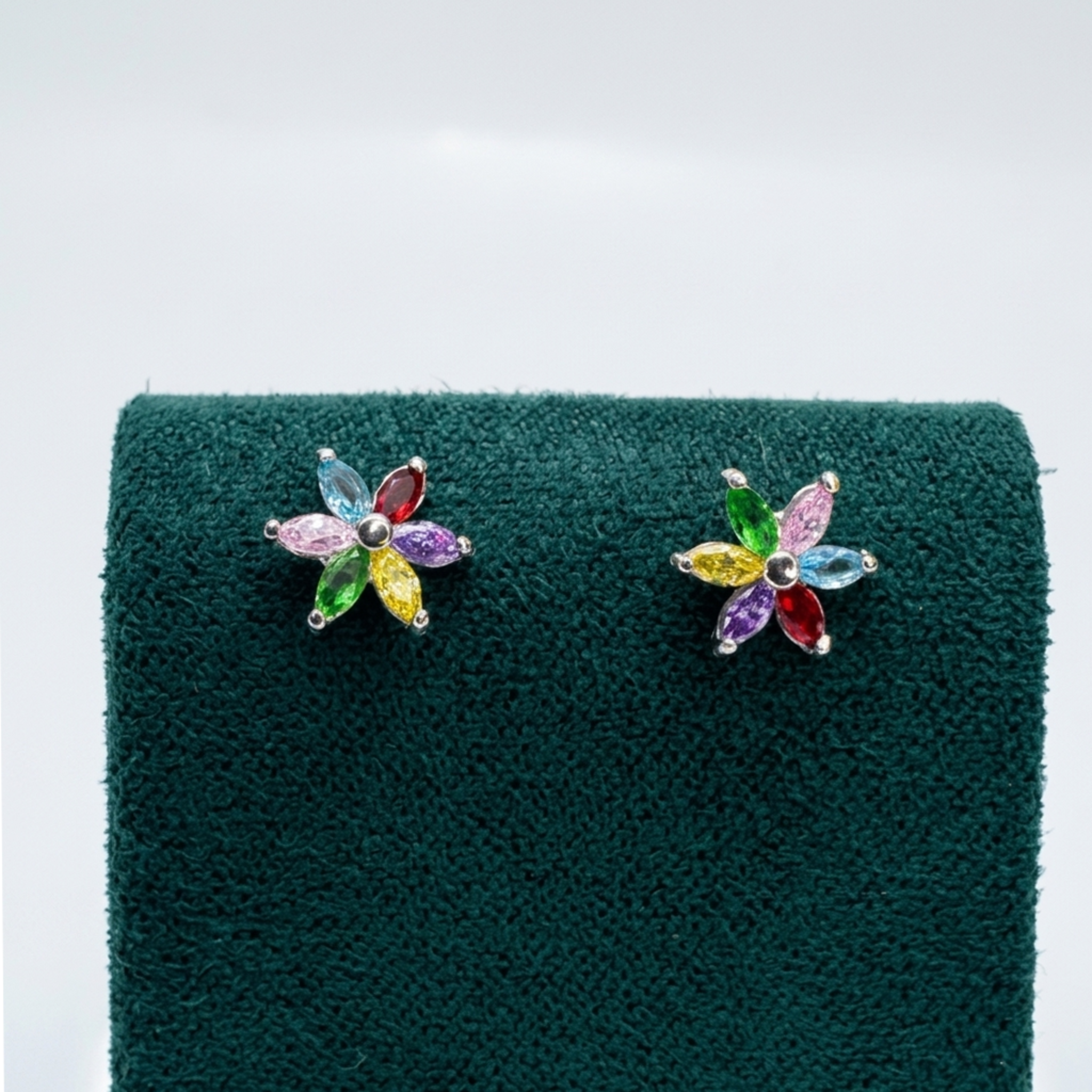 Nahaufnahme der luxuriösen Blüten-Ohrringe aus 925er Sterling Silber mit Rhodium-Anlaufschutz und farbenfrohem Zirkonia-Besatz auf einem edlen grünen Samtaufsteller.