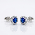 Zeitlose Damen-Ohrringe aus rhodiniertem 925er Silber im edlen Halo-Design mit strahlendem Steinkranz und blauen Zirkonia auf reinweißem Grund.