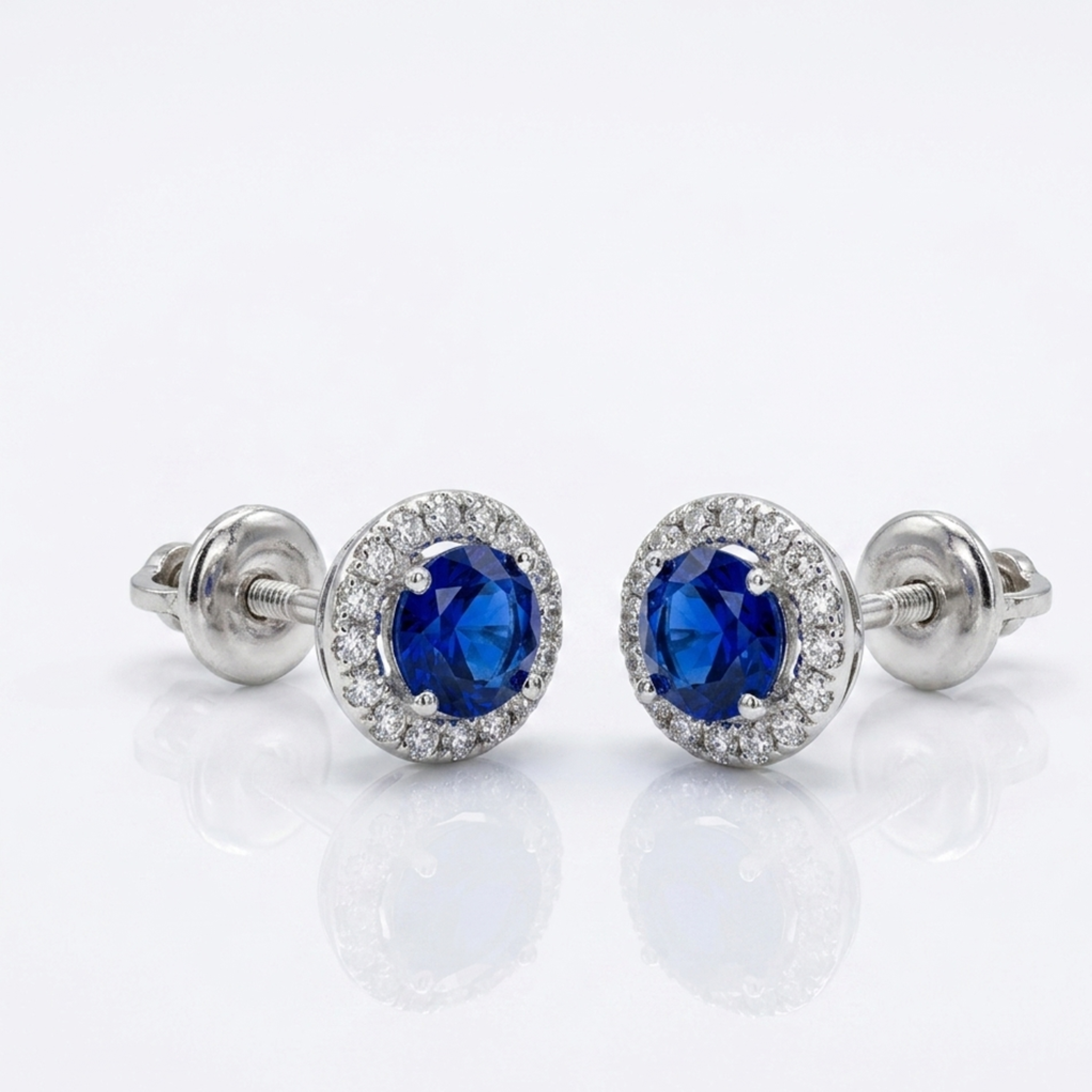 Zeitlose Damen-Ohrringe aus rhodiniertem 925er Silber im edlen Halo-Design mit strahlendem Steinkranz und blauen Zirkonia auf reinweißem Grund.
