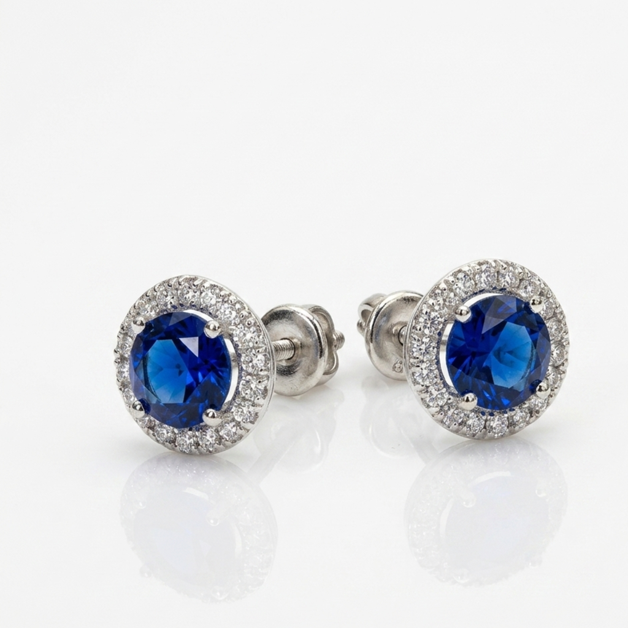 Detailaufnahme von runden Halo-Ohrsteckern aus 925 Silber mit intensiv saphirblauen Zentralsteinen auf weißem Hintergrund.