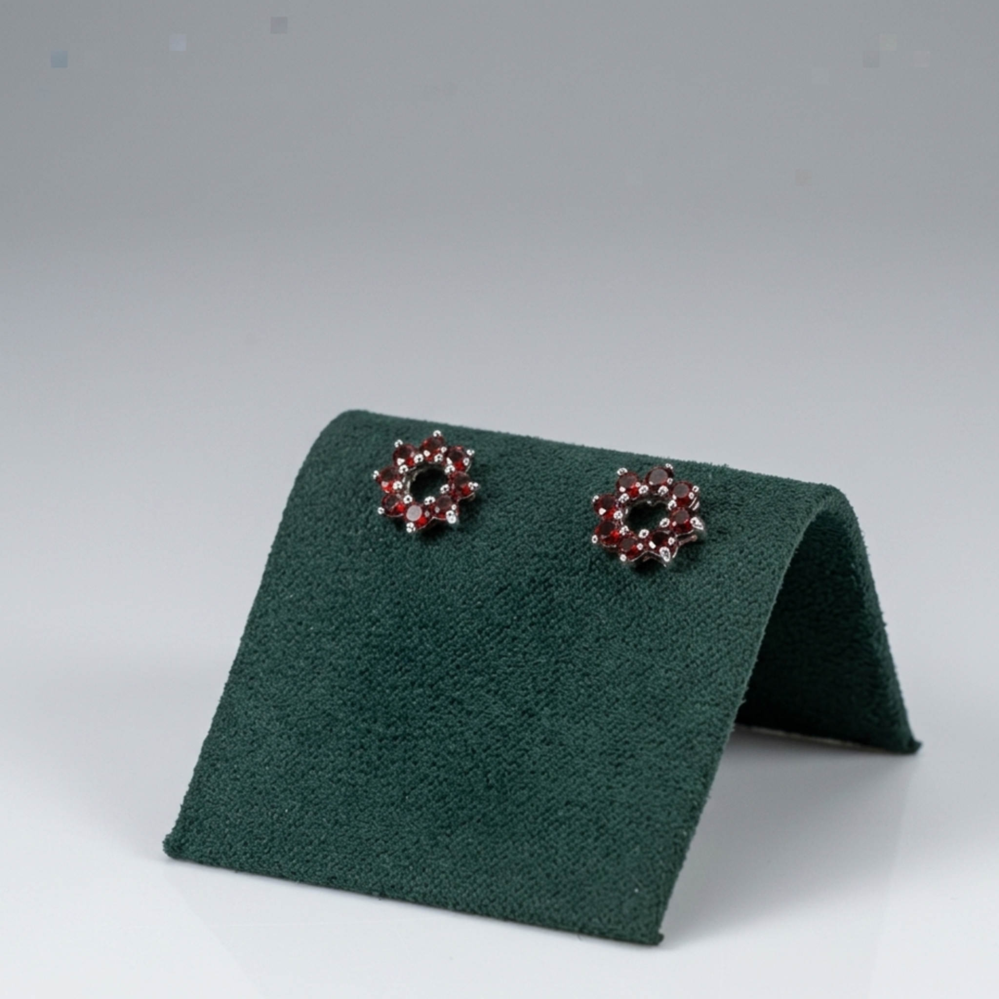 Edle Blumen-Ohrringe aus 925 Sterling Silber rhodiniert mit funkelnden roten Steinen auf einer eleganten grünen Samtpräsentation.