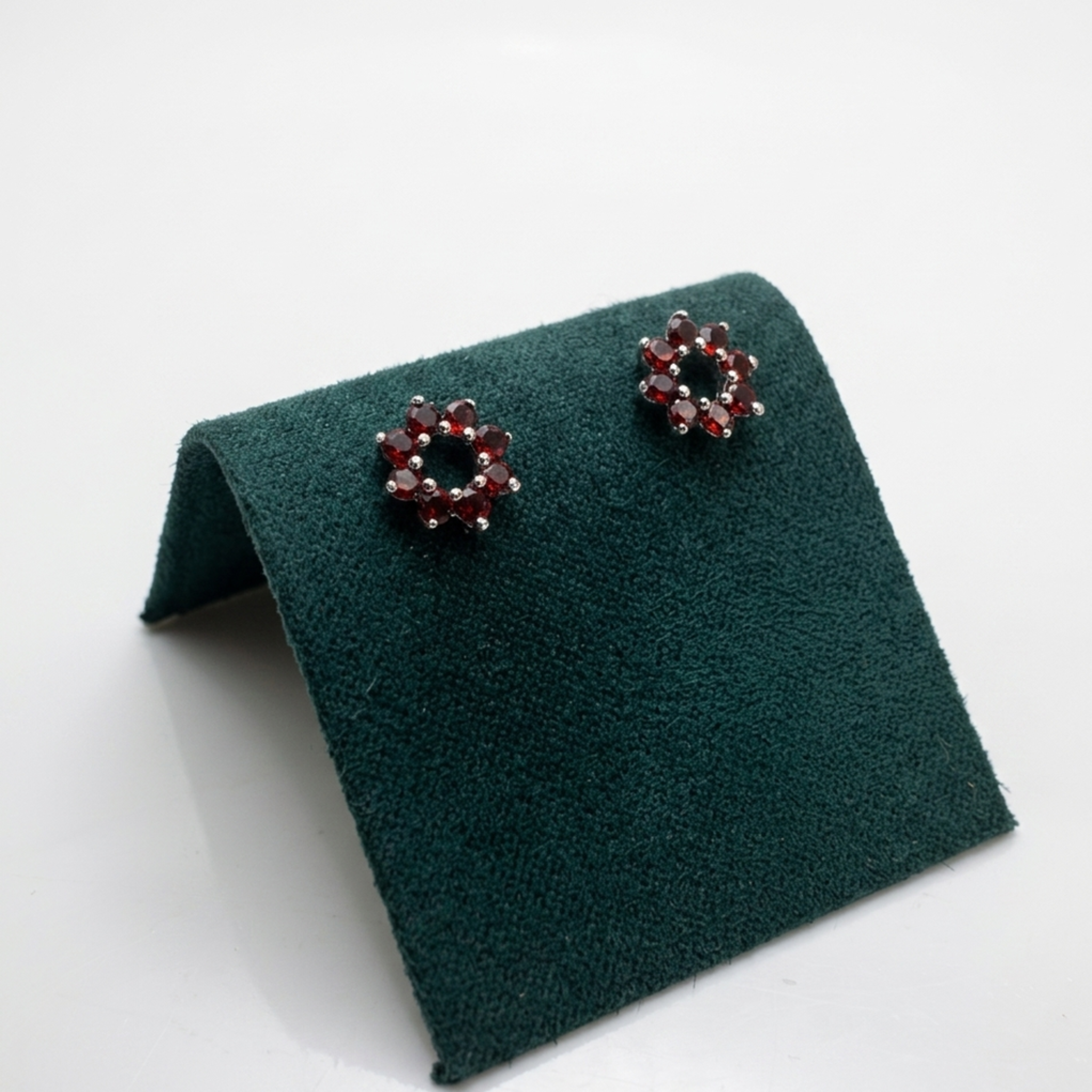 Elegante Präsentation der roten Blumen-Ohrstecker aus 925 Silber rhodiniert auf einem dunkelgrünen Samt-Display перед hellem Studiohintergrund.