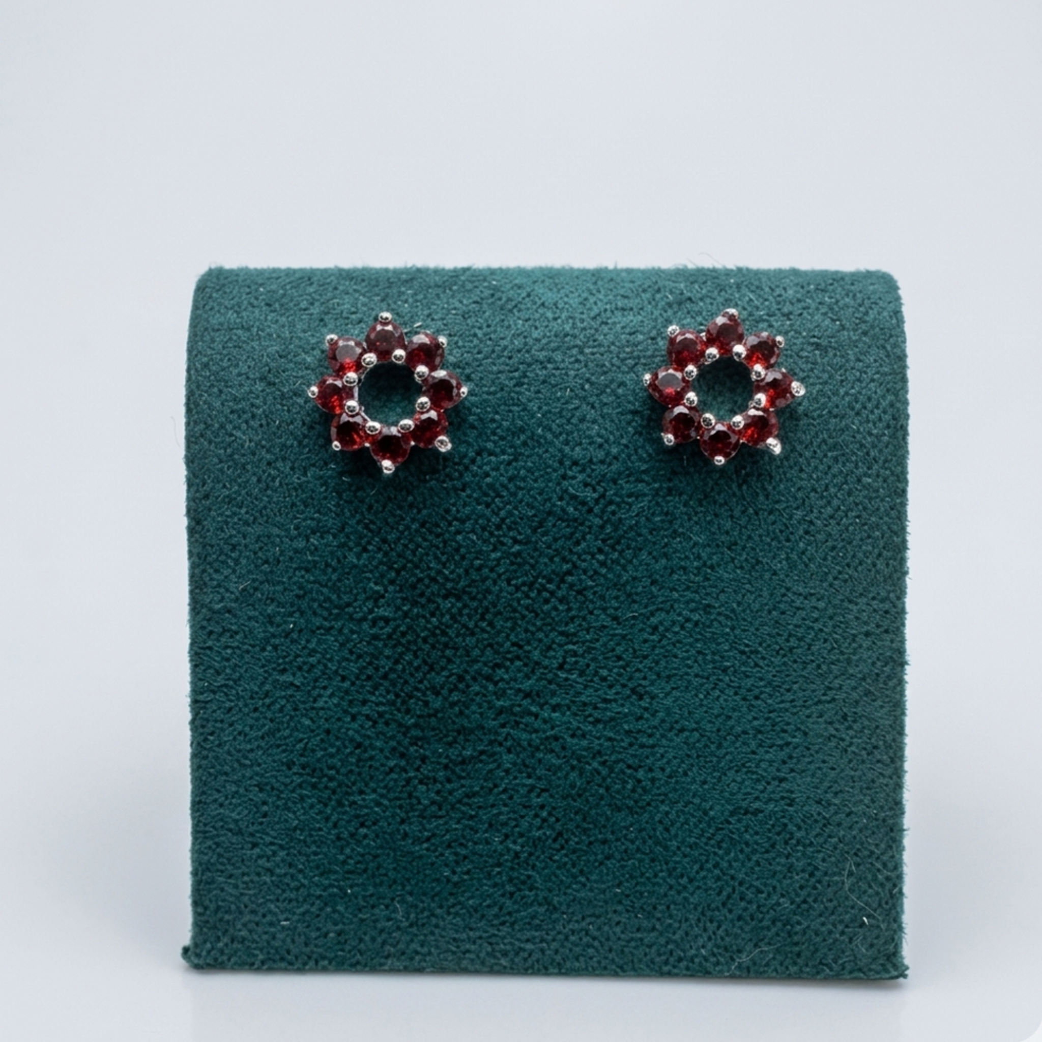 Handgefertigte Silber-Ohrstecker in Blumenform mit roten Zirkonia-Steinen, präsentiert auf einem grünen Samt-Display.
