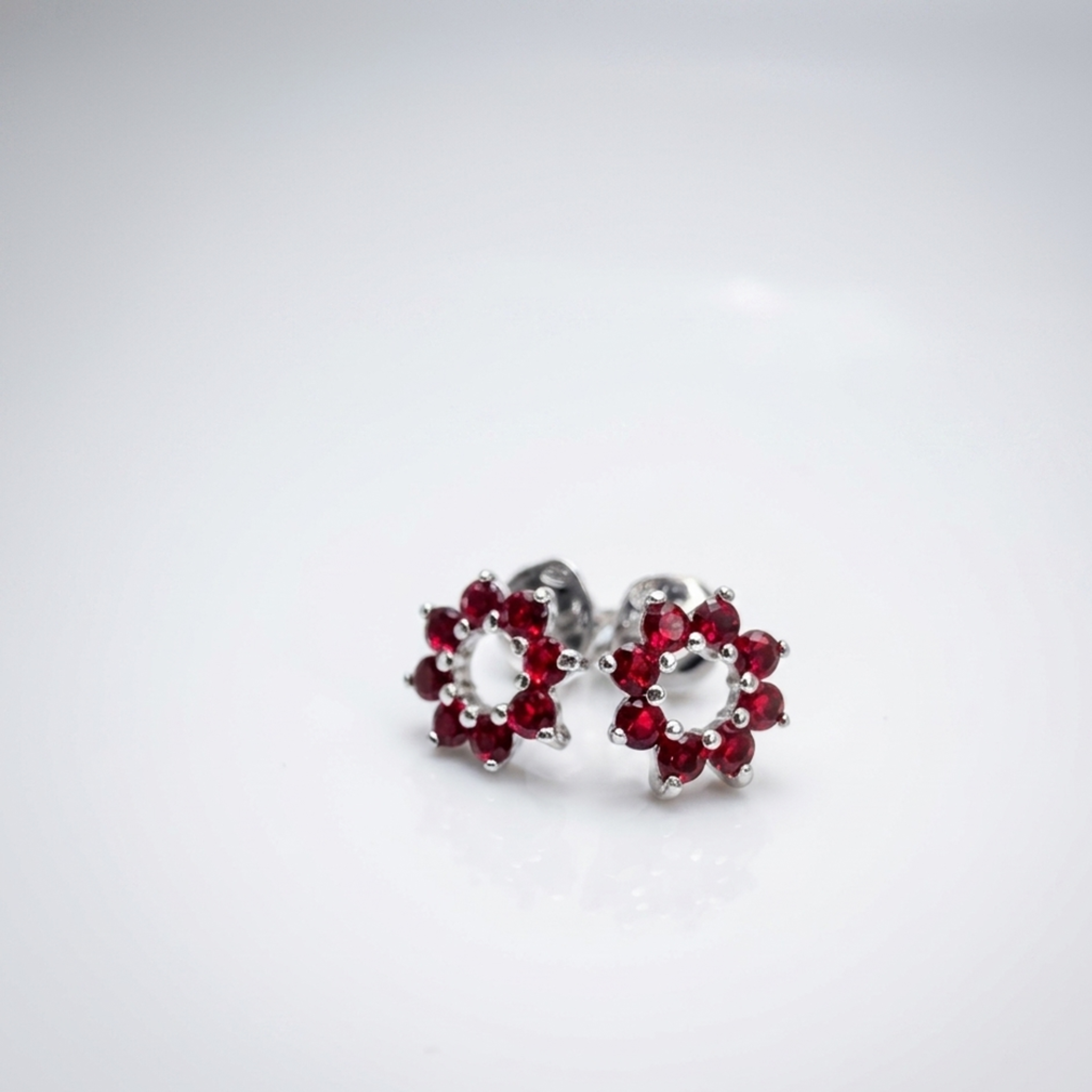 Premium Silber-Ohrstecker „Blume“ aus 925 Sterling Silber rhodiniert mit roten Zirkonia-Steinen auf weißem Hintergrund.