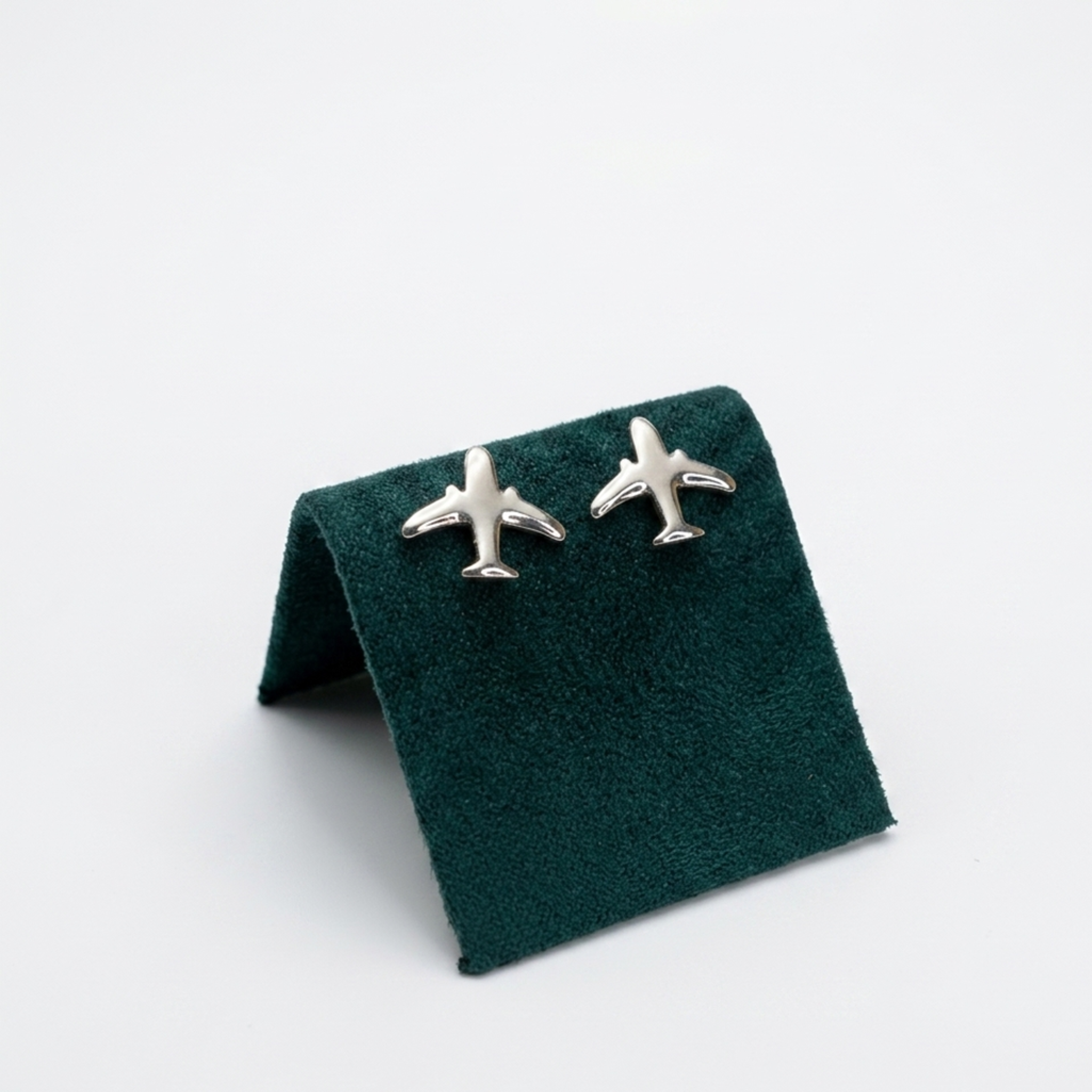 Originelle Flugzeug-Ohrstecker aus 925er Silber, rhodiniert, im minimalistischen Design, elegant präsentiert auf einem dunkelgrünen Samt-Display.