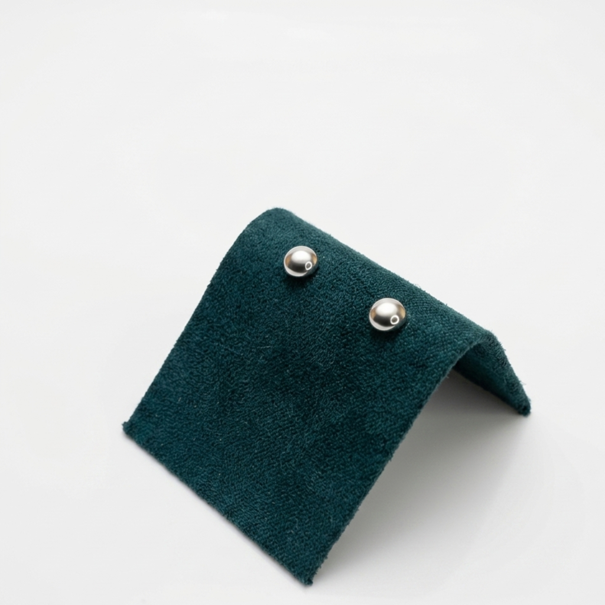 Zeitloser Designerschmuck: Rhodinierte Silberohrringe in Kugelform ohne Steine auf einer exklusiven dunkelgrünen Samtpräsentation.
