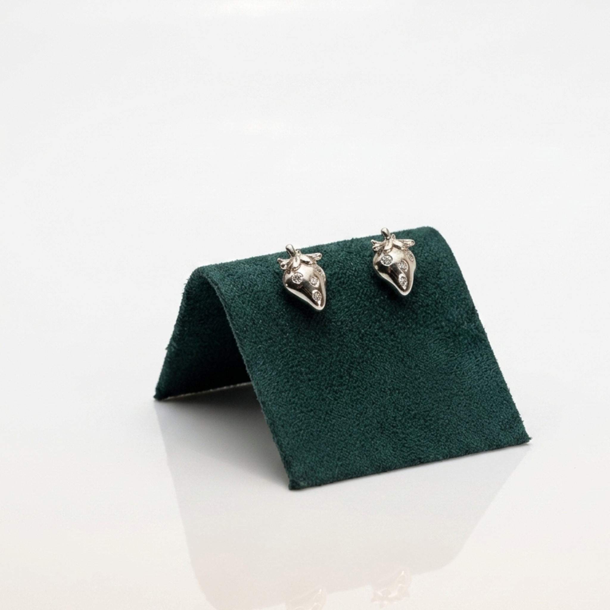 Handgefertigter Designerschmuck: Rhodinierte Motiv-Ohrringe "Erdbeere" aus 925 Sterling Silber mit punktuellem Zirkonia-Besatz auf einer exklusiven dunkelgrünen Samtpräsentation.