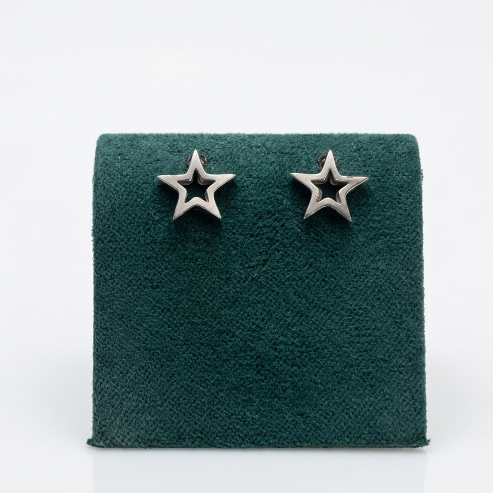 Nahaufnahme der Vorderansicht von offenen Sterne-Ohrringen aus glänzendem Silber auf einem edlen grünen Samtaufsteller.