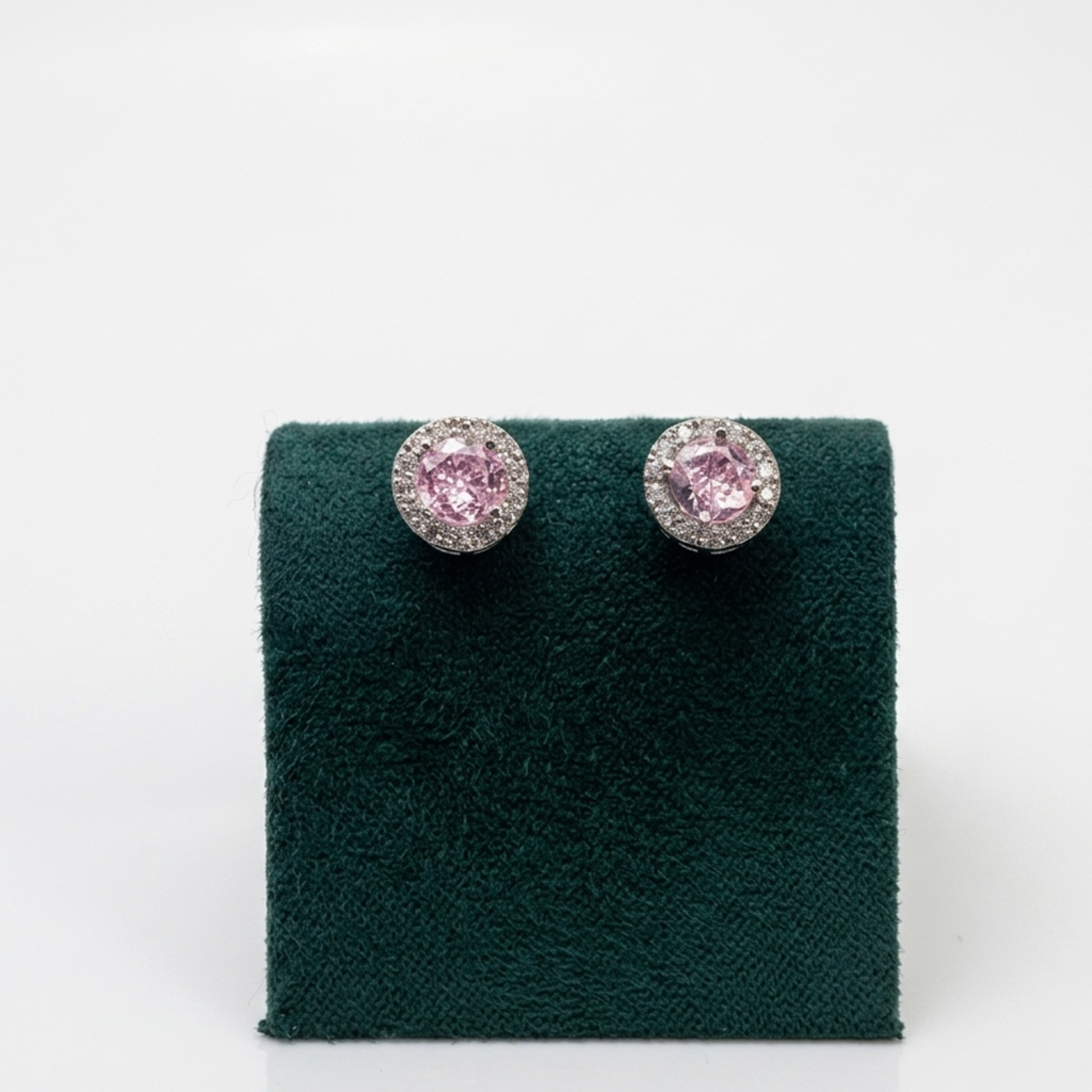 Nahaufnahme der Vorderansicht von edlen ovalen Silberohrringen mit einem großen rosa Zirkonia-Zentralstein auf einem grünen Samtaufsteller.