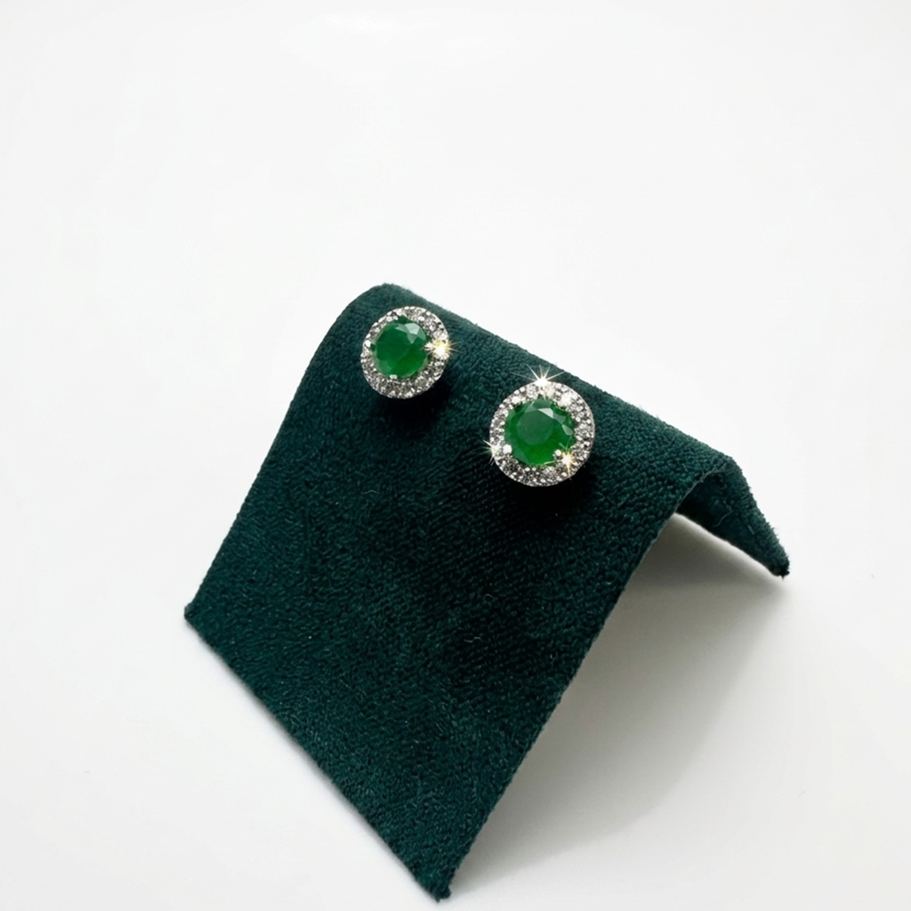 Handgefertigter Designerschmuck: Rhodinierte Solitär-Ohrringe mit smaragdgrünen Zirkonia-Zentralsteinen auf einer exklusiven dunkelgrünen Samtpräsentation.