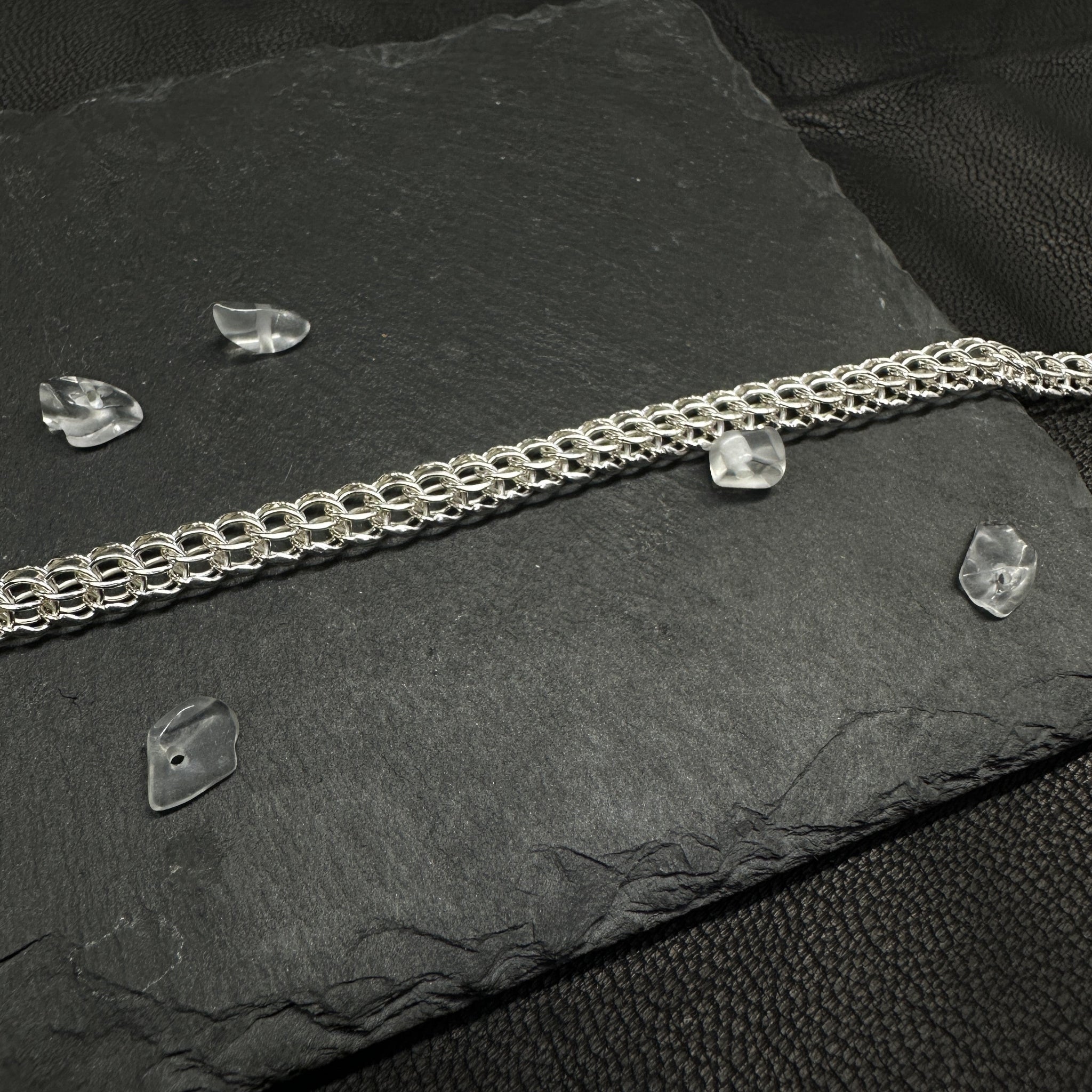 Detailansicht einer in Handarbeit gefertigten Halskette „Python“ aus glänzendem 925er Silber. Das detailreiche Geflecht liegt im Fokus auf dunklem Schiefer-Untergrund.