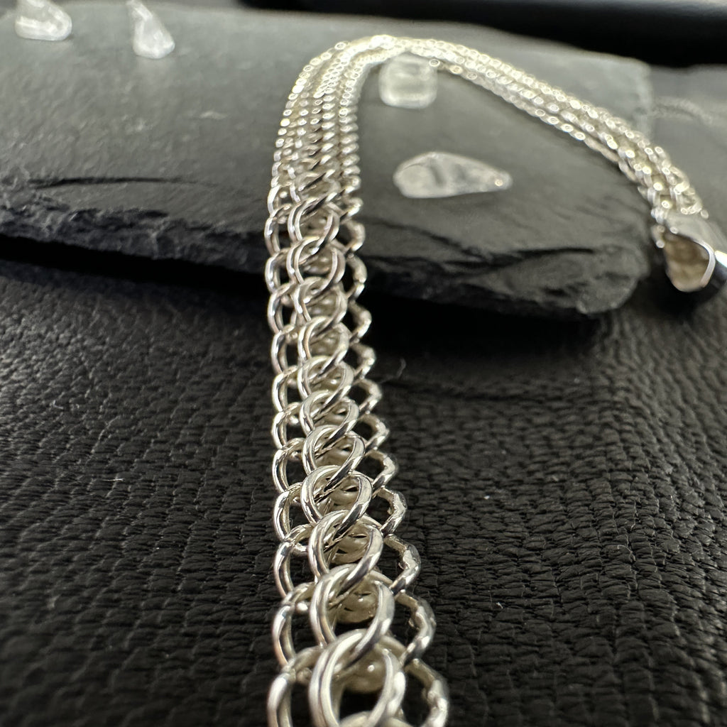 In Handarbeit gefertigte Halskette „Python“ aus glänzendem 925er Silber. Das feine, breite Geflecht liegt im Fokus auf dunklem Schiefer und Leder-Hintergrund.
