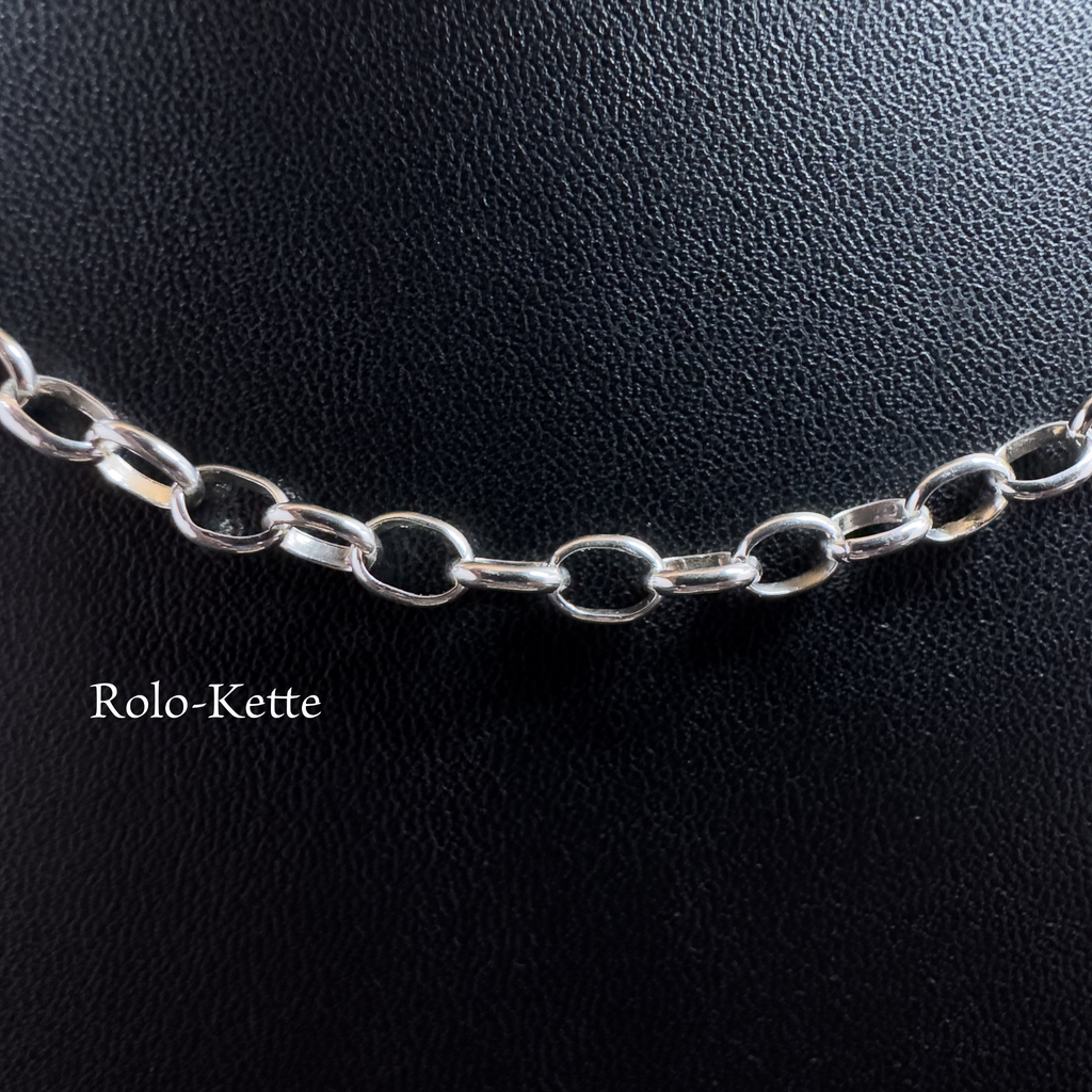 Nahaufnahme einer filigranen Rolo-Kette aus glänzendem 925er Silber auf schwarzem Lederhintergrund mit dem Schriftzug Rolo-Kette.