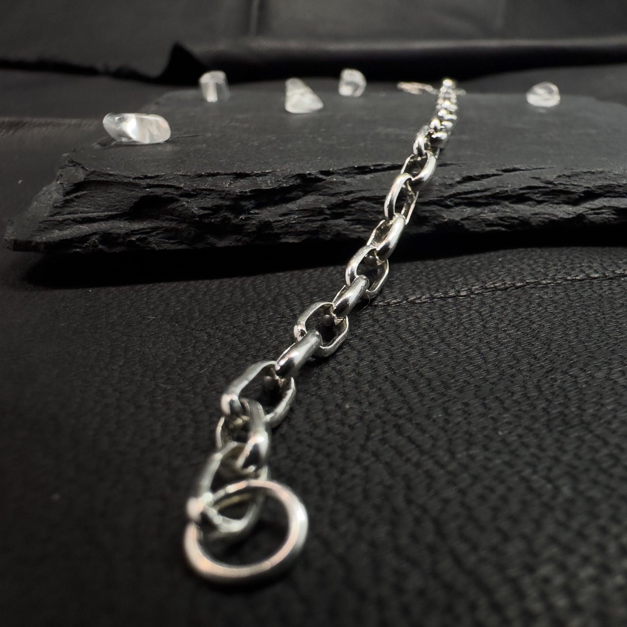 Produktfoto einer Rolo-Kette (Ankerkette) aus 925er Silber in perspektivischer Ansicht, liegend auf dunklem Schiefergestein mit kleinen Deko-Kristallen im Hintergrund.