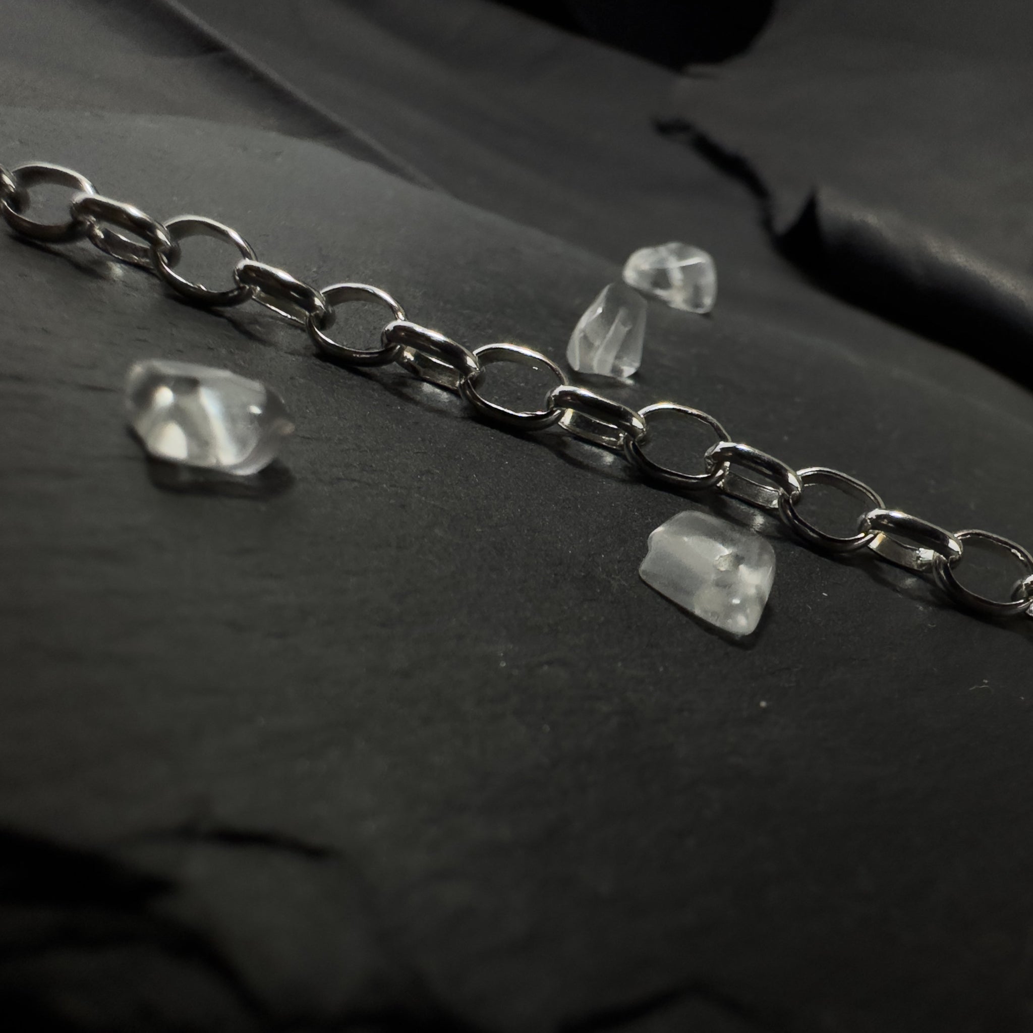 Detailaufnahme einer silbernen Gliederkette im Rolo-Stil, die sich von einem runden Endring im Vordergrund über eine strukturierte, dunkle Steinfläche nach hinten erstreckt.