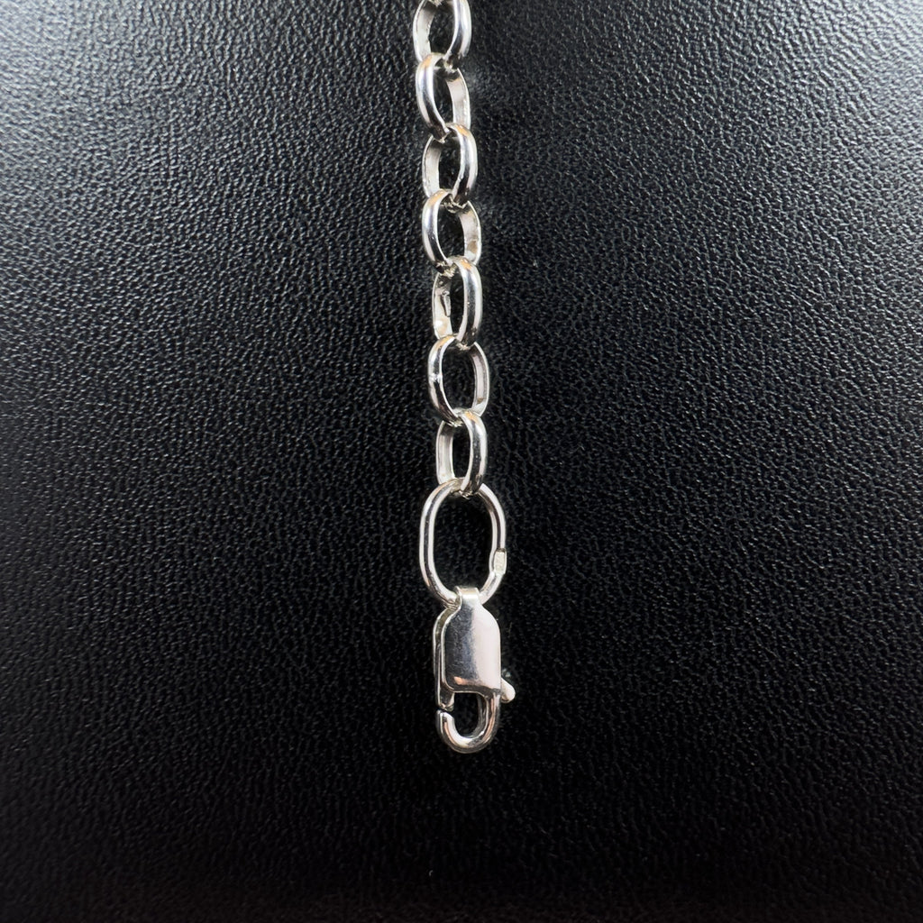 Detailaufnahme einer silbernen Gliederkette im Rolo-Stil, die sich von einem runden Endring im Vordergrund über eine strukturierte, dunkle Steinfläche nach hinten erstreckt.