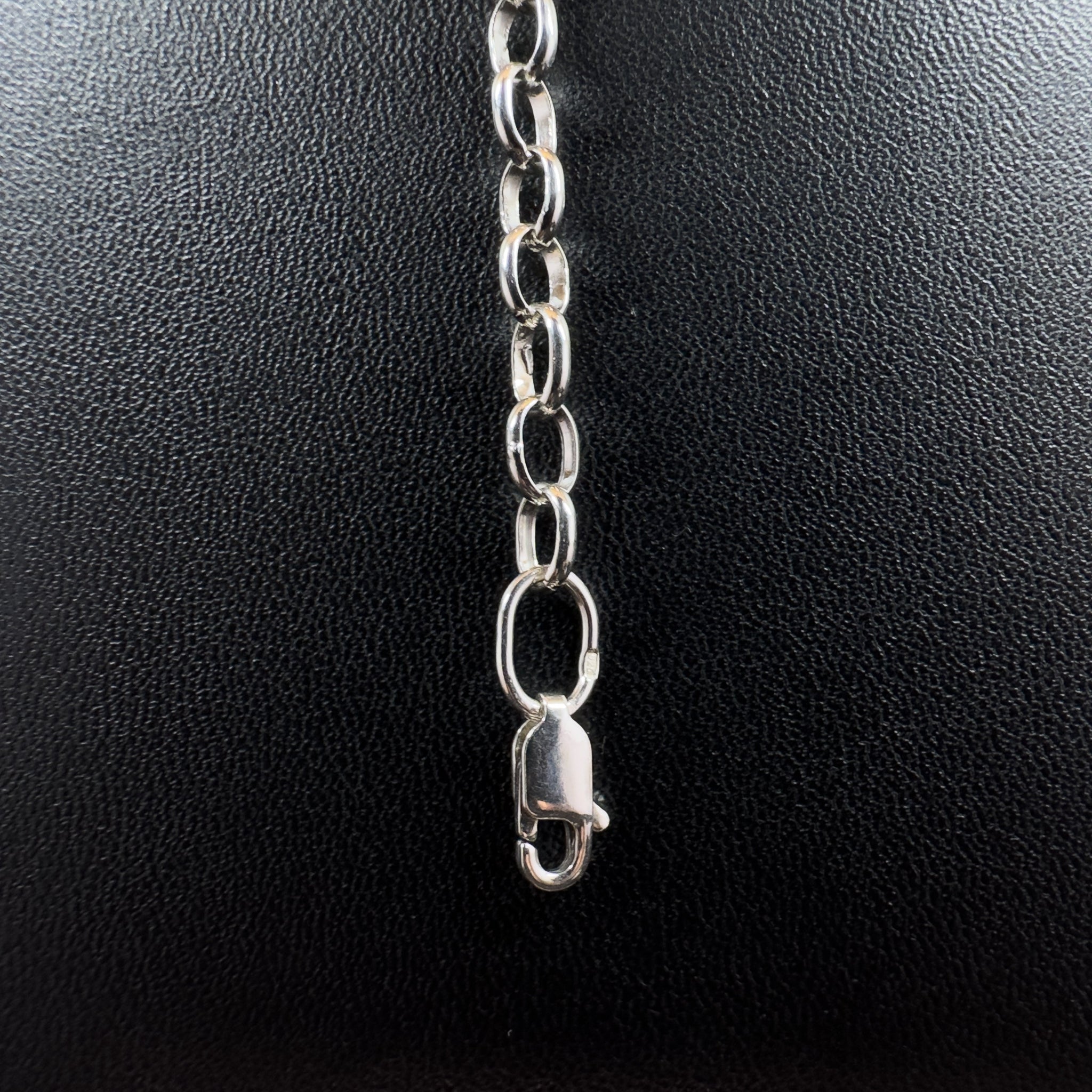 Detailaufnahme einer silbernen Gliederkette im Rolo-Stil, die sich von einem runden Endring im Vordergrund über eine strukturierte, dunkle Steinfläche nach hinten erstreckt.