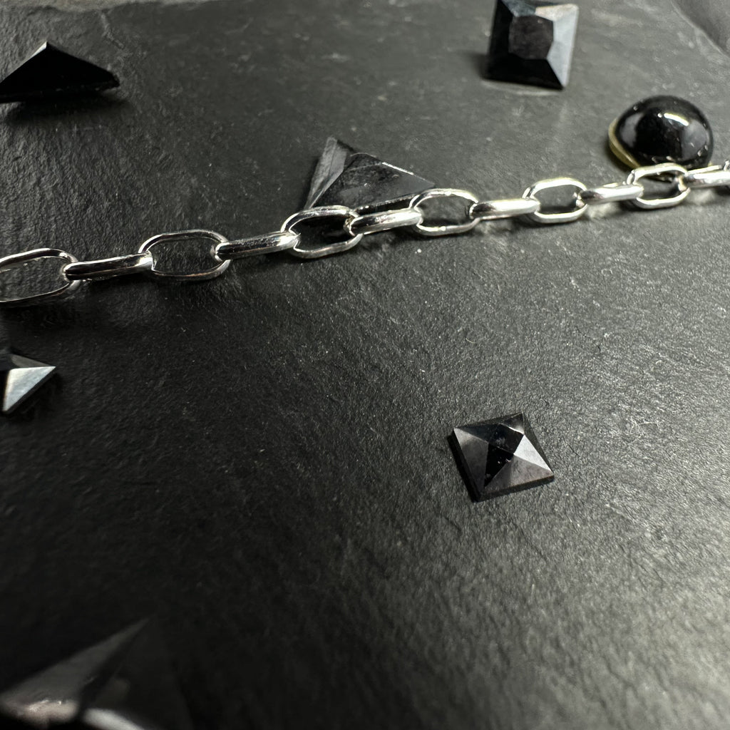 Makroaufnahme einer Rolo-Kette (Ankerkette) aus 925er Silber auf einer dunklen Steinoberfläche, dekoriert mit kleinen, pyramidenförmigen schwarzen Schmuckelementen.