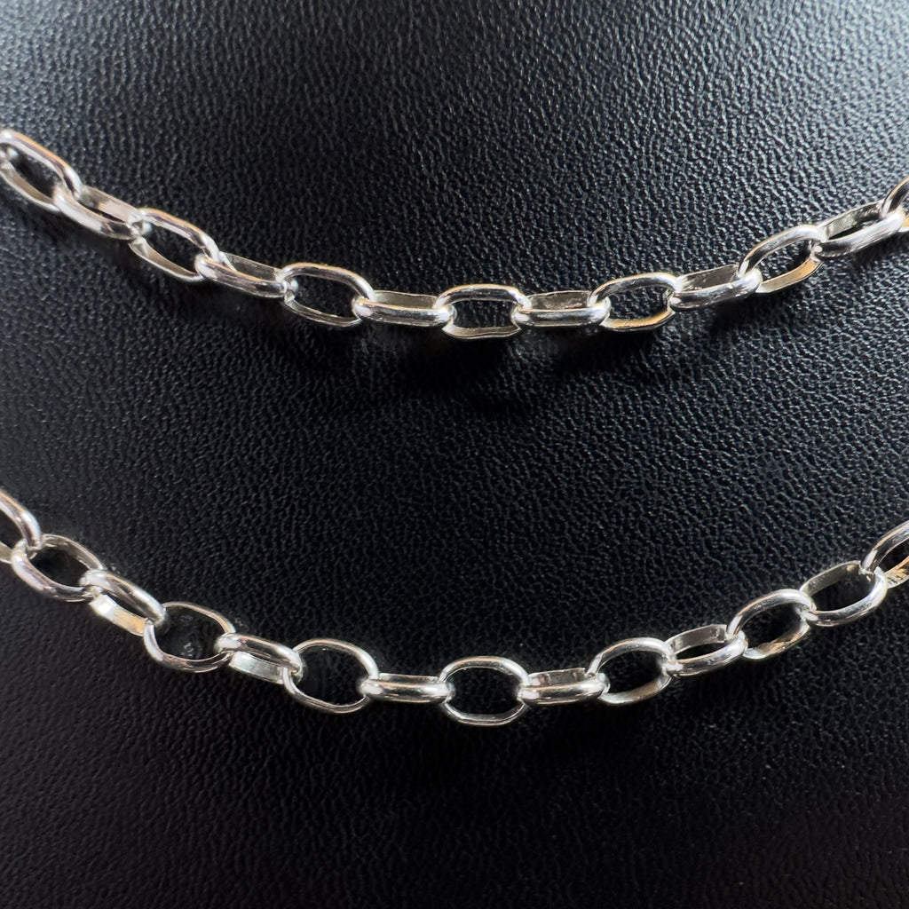 Detailansicht der polierten, ovalen Kettenglieder einer silbernen Gliederkette im Rolo-Stil vor einem dunklen Kunstleder-Hintergrund.