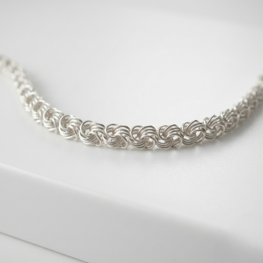 Detailaufnahme einer feinen Rose-Gliederschmuck aus 925er Silber, die in S-Form auf einer weißen Oberfläche liegt.