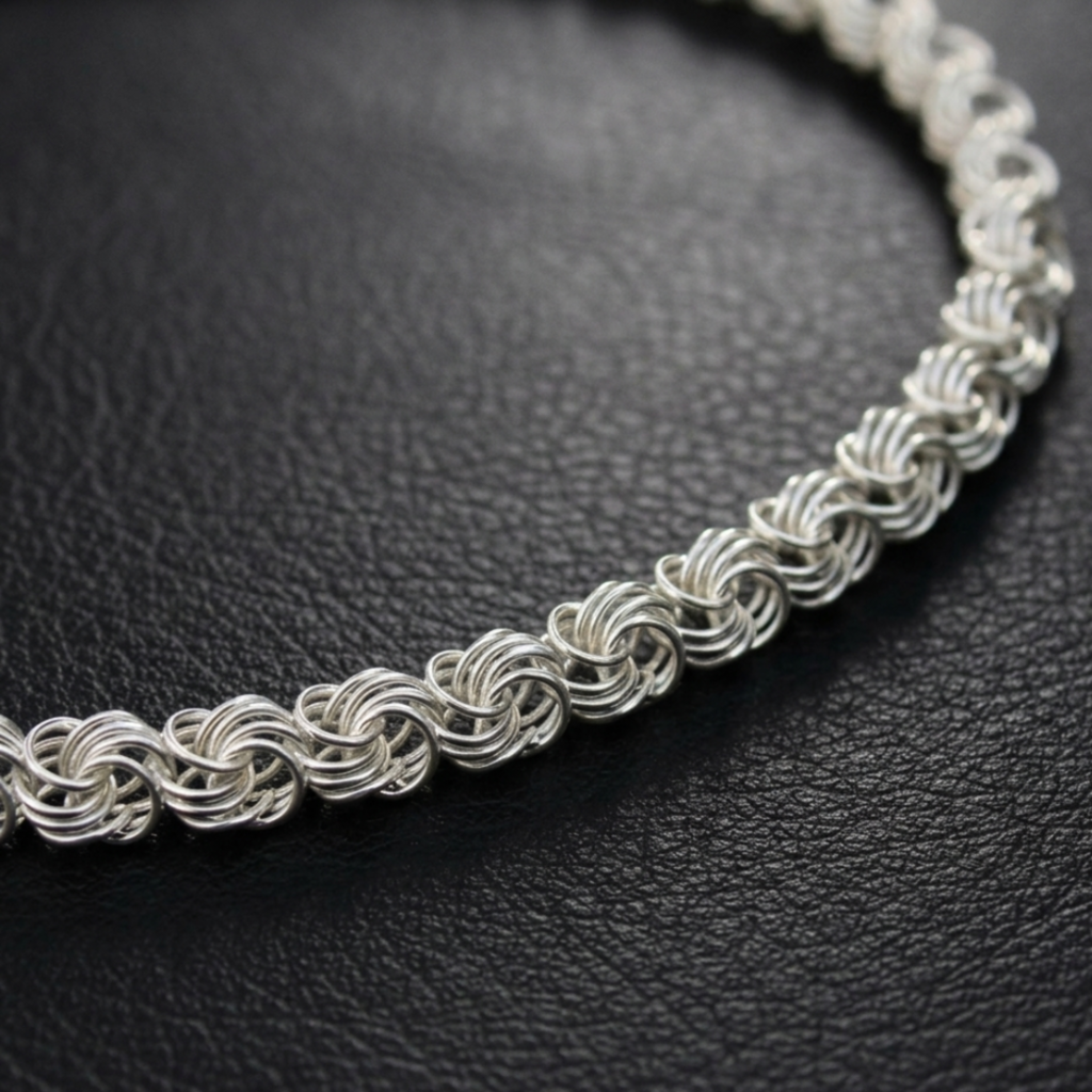 Detailaufnahme einer feinen Rose-Gliederschmucks aus 925er Silber, die im Halbkreis auf einer dunklen Leder-Oberfläche liegt.