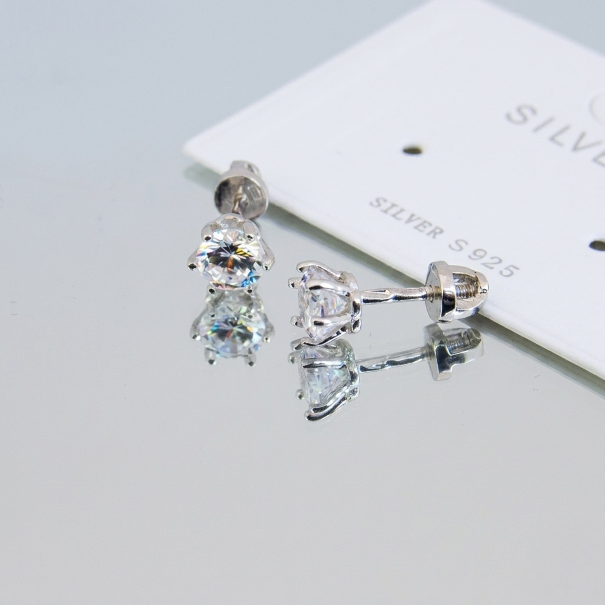 Handgefertigte Silber-Ohrstecker aus 925 Sterling Silber rhodiniert mit funkelndem 5mm Zirkonia und Schraubverschluss auf einer Spiegeloberfläche.