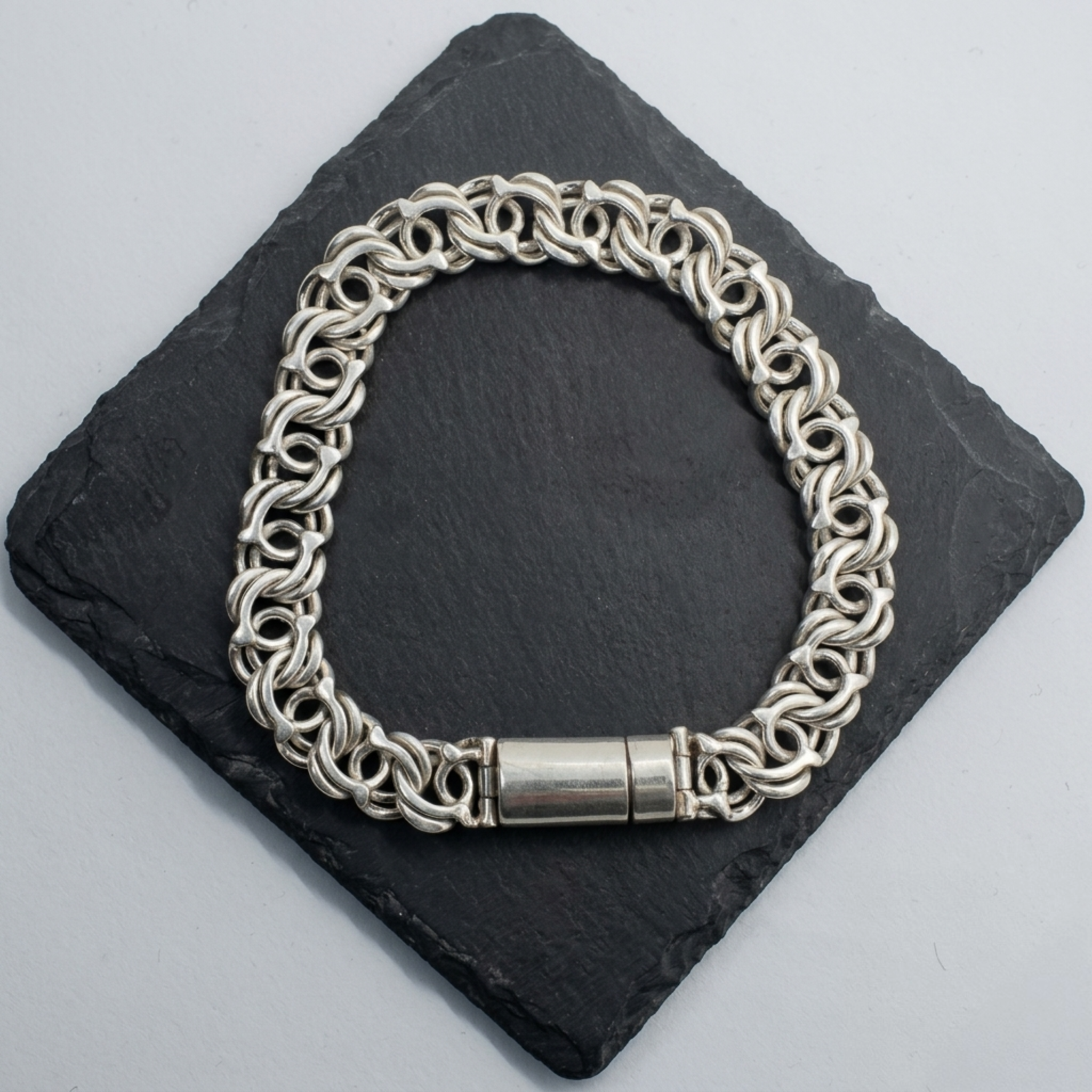 Detailaufnahme der Rückseite eines handgearbeiteten 925er Sterling Silberarmbands zur Veranschaulichung des glatten Zylinder-Verschlusses auf dunklem Stein.